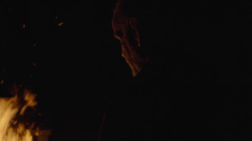 Old man stands in front of the camp fire and look at it at night