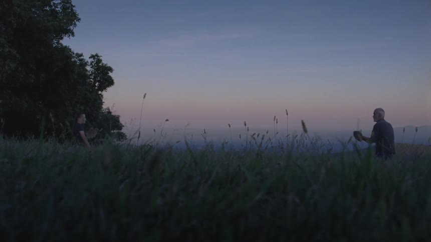 Two men throw and catch small ball in the forest at dusk