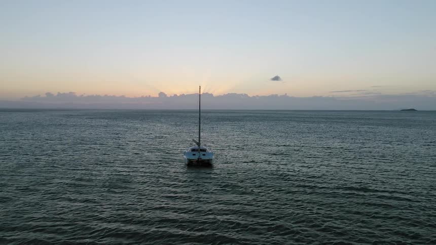 An anchored sailboat with sail down bobs on the water at sunset