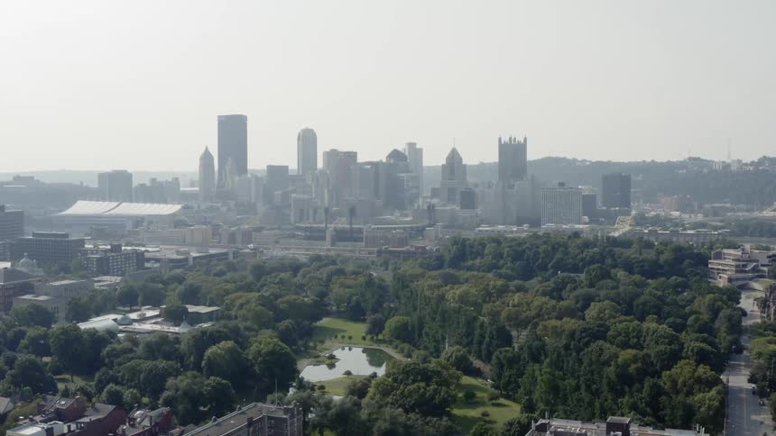 Trees and pond of a city park with skyscrapers in a city skyline in the distance