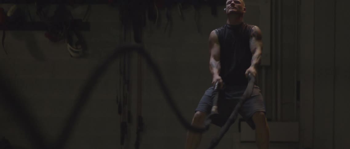 A man shakes large heavy ropes up and down