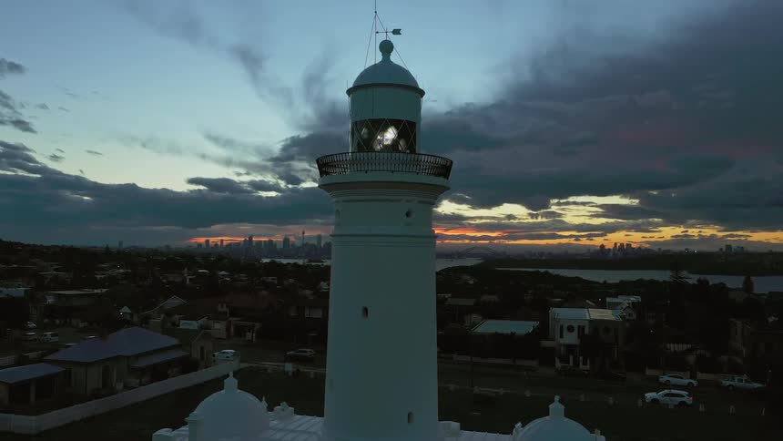 A light turns in the lantern panel of a white lighthouse at sunset