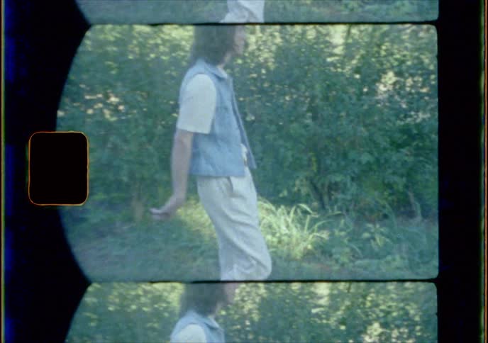 A man walks through the grass by a wood pile