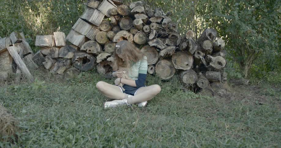 Young girl sitting on the grass against a stack of lumbar cuddling a kitten