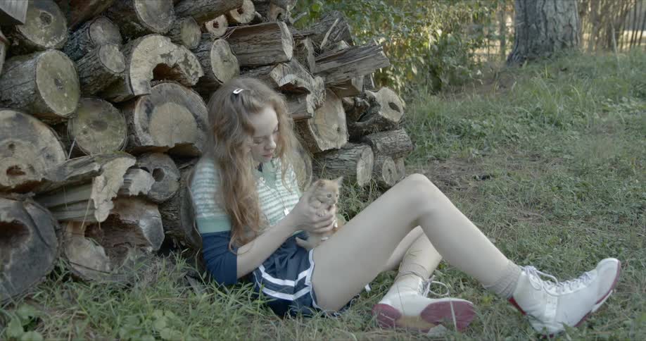 A woman holds an orange kitten next to a pile of wood
