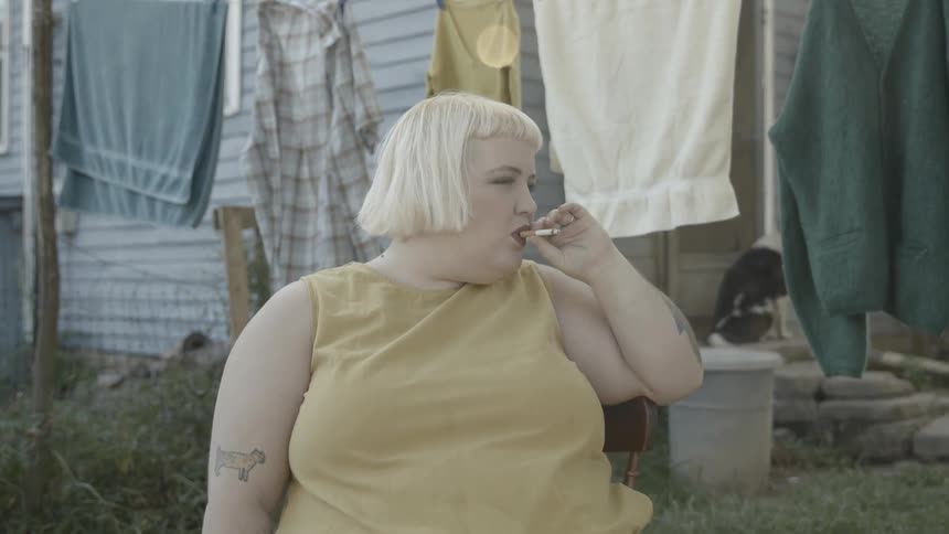 Woman sits near hanging laundry smoking