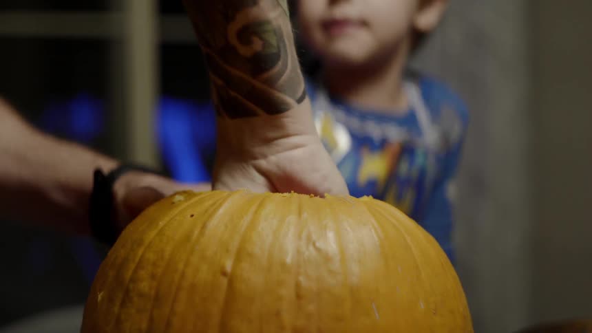 A white person uses a tool to dig around inside a pumpkin
