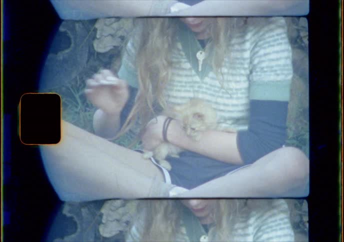 Young girl sitting on the grass near a stack of lumbar cuddling a kitten
