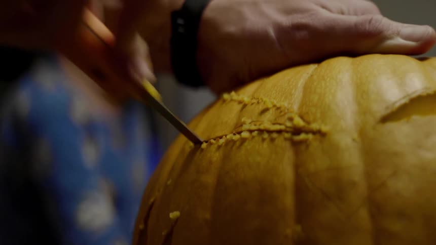 Person carves jack o lantern while child watches