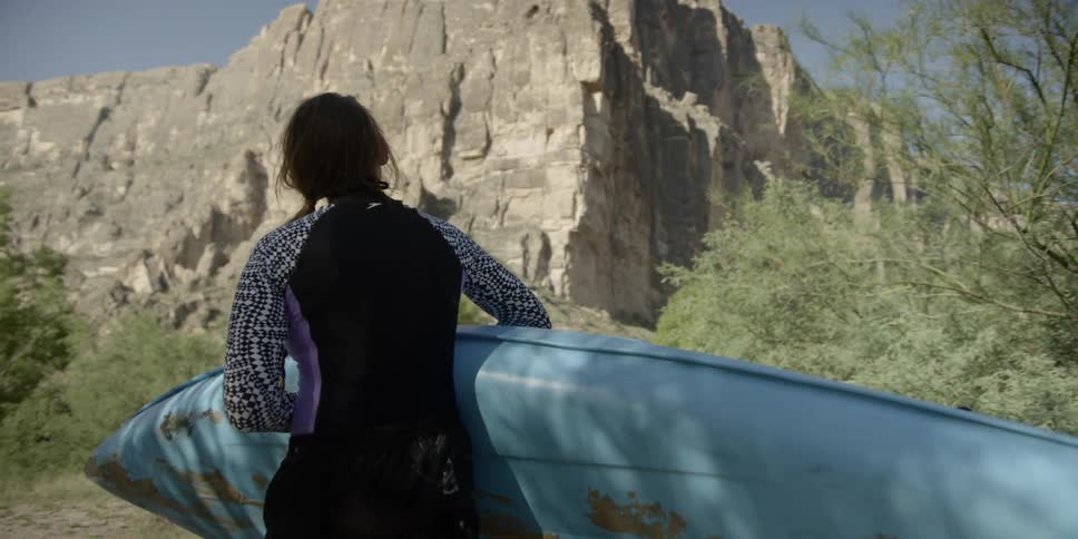 A white woman carries a kayak along a dirt path