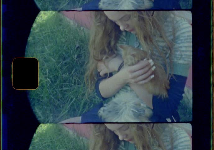 Blonde girl holds and pets kitten on the grass in front of red painted wall