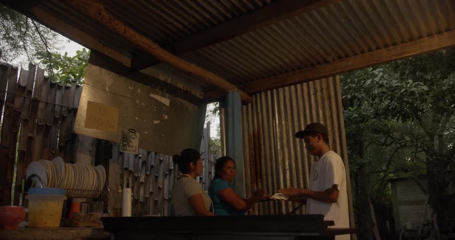 A young man helps two females with domestic work in a shelter in a tropical location