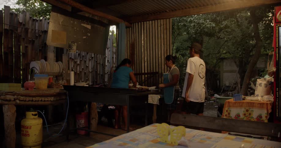 Three people preparing food in a rustic building made from bamboo and corrugated plastic