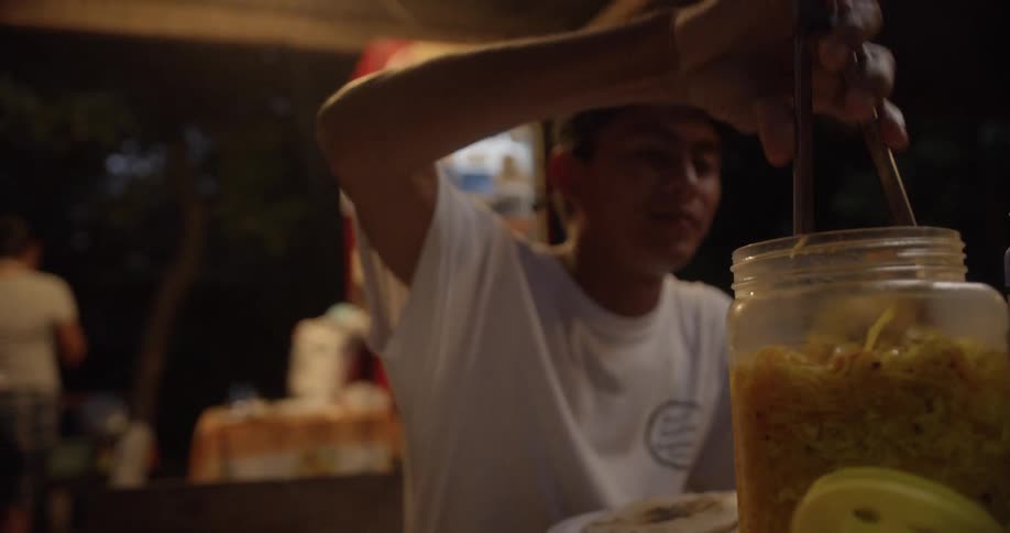 A man smiles as he uses tongs to reach into a jar and put food on his plate