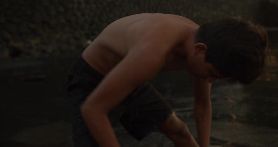 A boy stretches and touches his toes next to a flowing stream