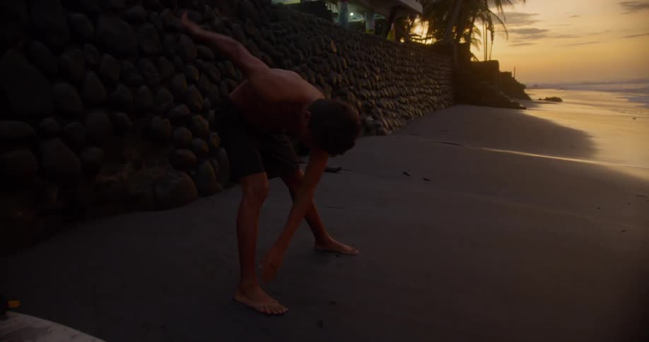 Young boy stretching on a sandy beach near the shoreline at sunrise