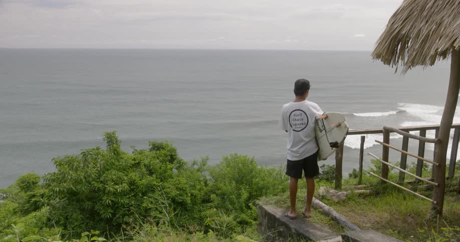 Surfer walking out to check out the waves below from a balcony on an island