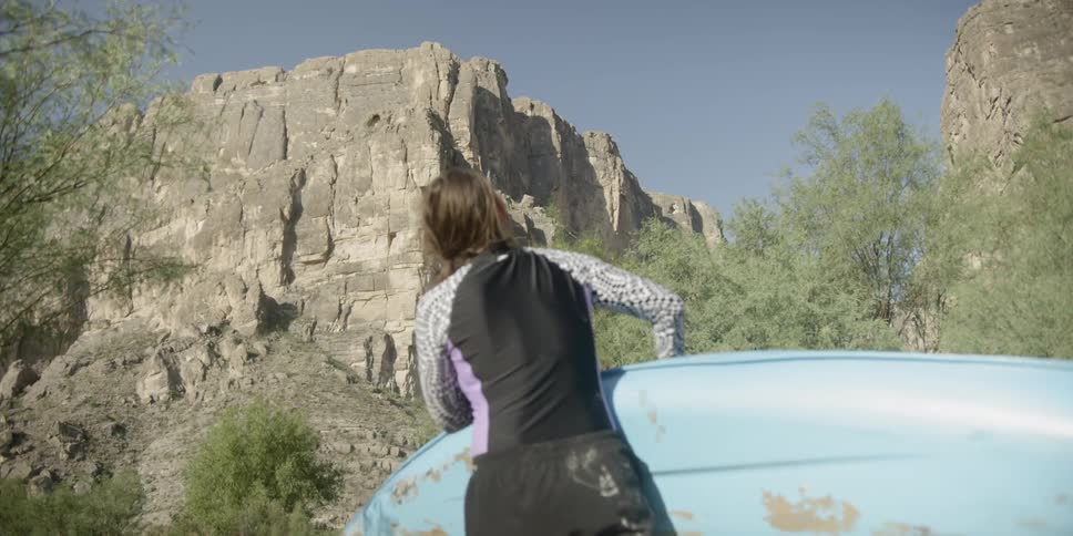 A woman is carrying a boat and looking at a cliff outdoors