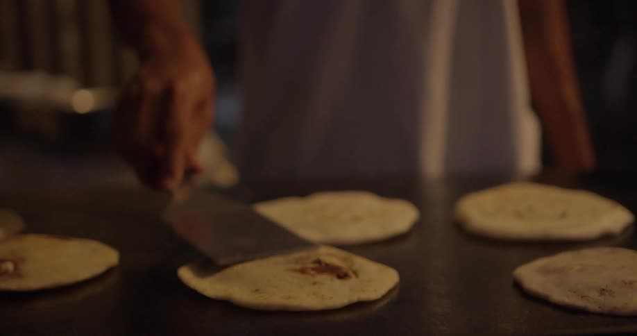 A cook flips circles of dough on a grill