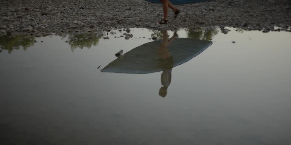 A person walks near a puddle carrying a kayak