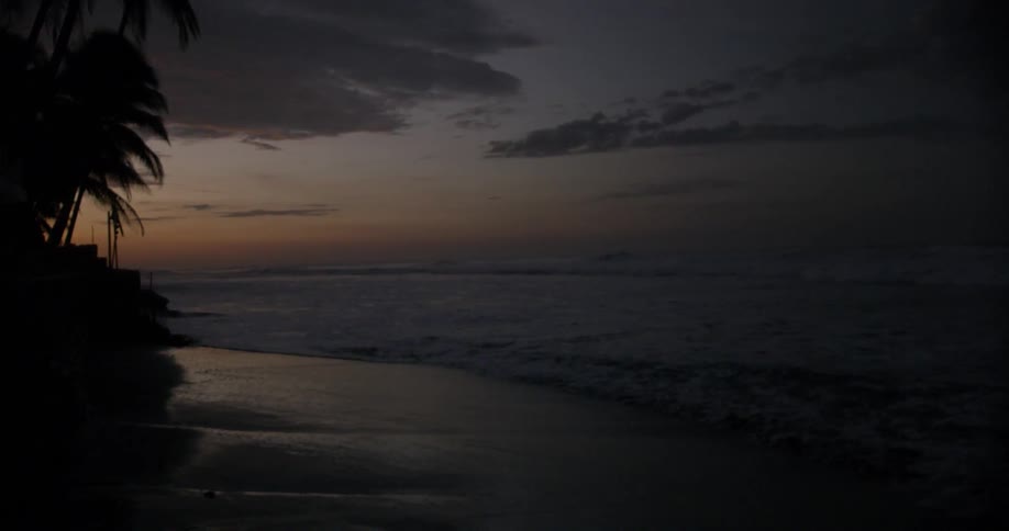 A view of gentle waves moving in on a sandy beach at dusk