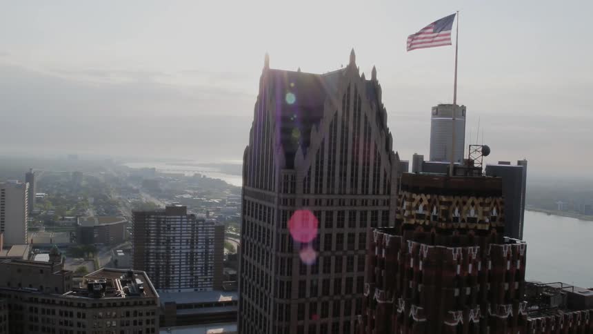An american flag flies over the top of a all skyscraper in a city