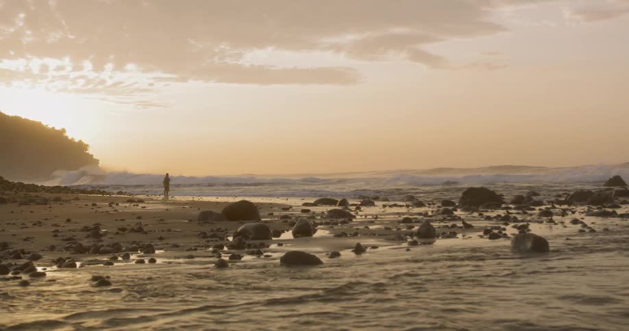 A person standing on a rocky beach at sunset