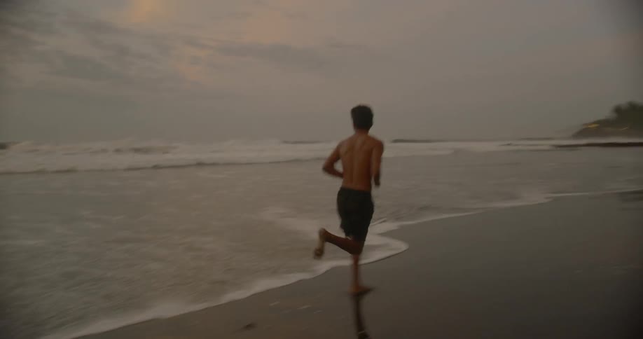 Young male running on the beach near the shoreline at sunrise