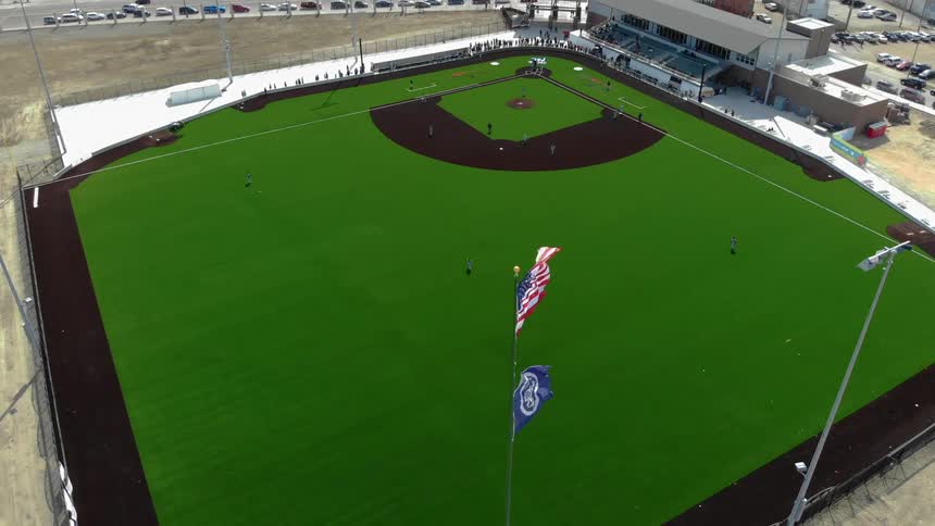 An american flag flies atop a flag pole at a baseball field
