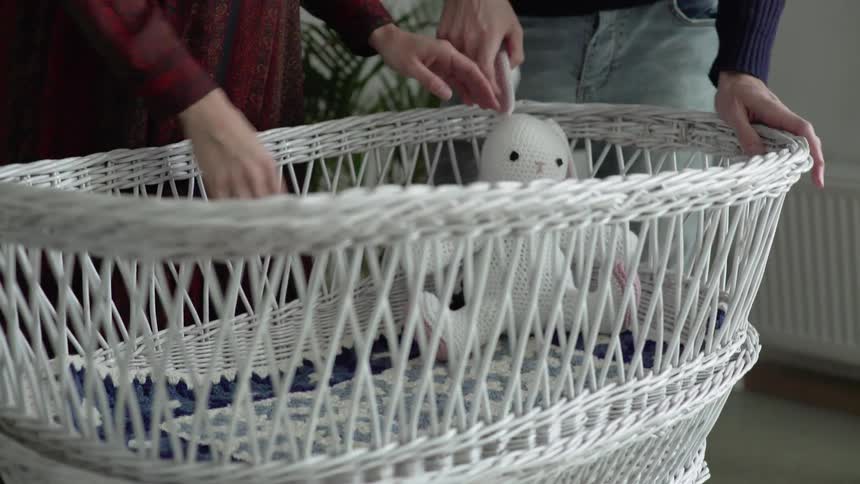 A man and a woman put a stuffed animal into a wicker bassinet