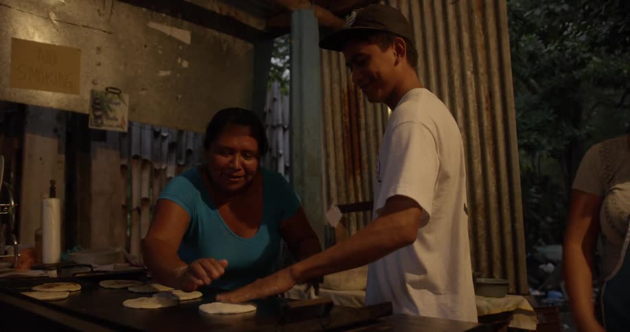 A cook puts dough on a grill with some help from a couple of women