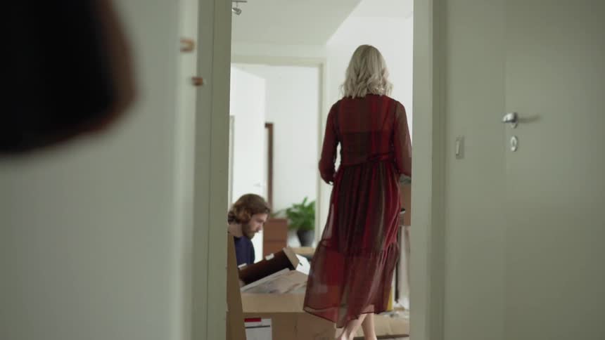 The woman in the red dress carries the box into where the man is