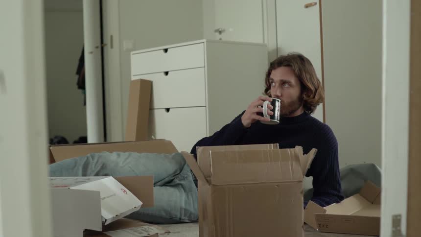 A man lays on the floor with a coffee cup surrounded by opened boxes