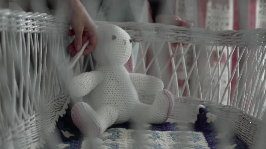 A knitted stuffed bunny inside of a wicker bassinet with a knitted blanket inside