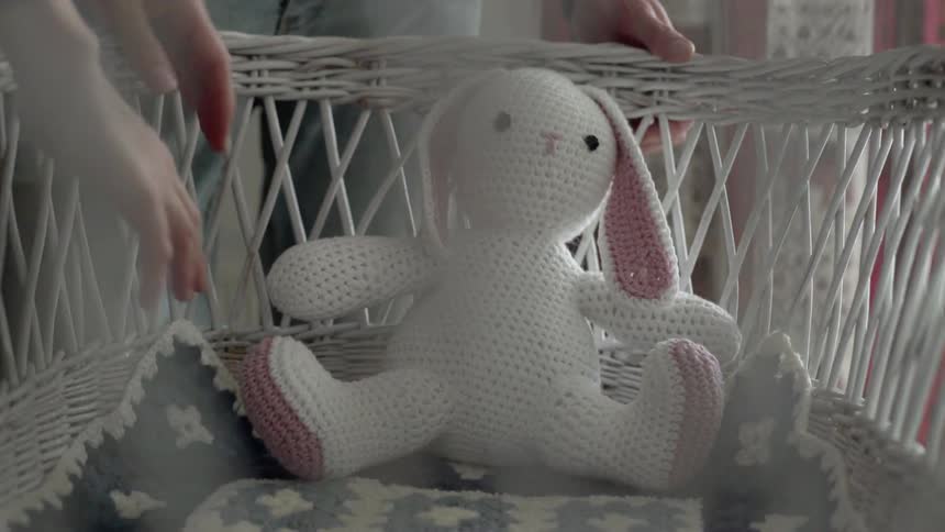 A person putting a plush toy rabbit in a bassinet