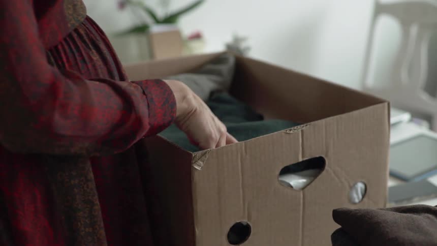 Pregnant woman wearing red dress takes folded clothes out of box during daylight