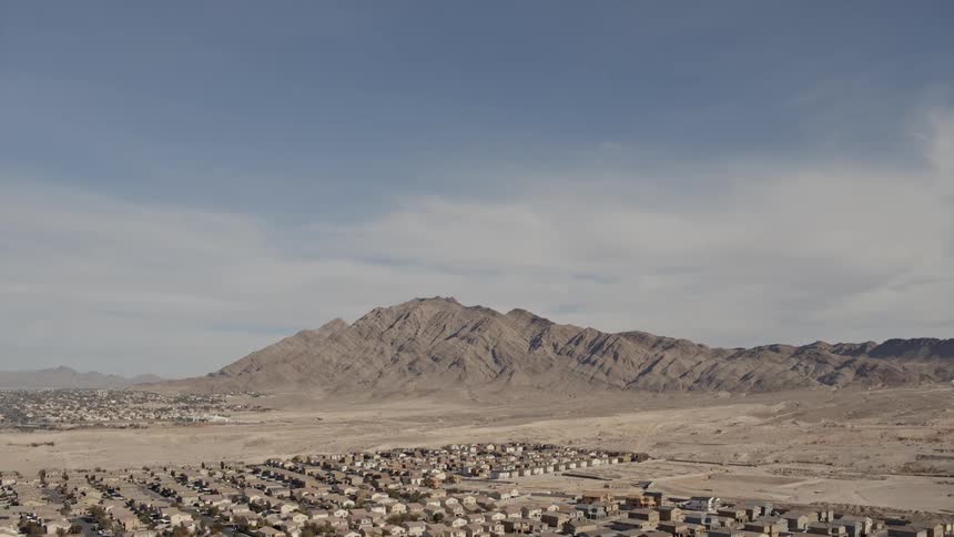 A fairly small housing community is surrounded by dirt in a rural area with a small mountain range in the background