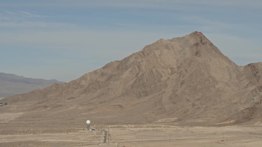 Some sort of structure with a large white globe on top is in the middle of nowhere with a large dirt hill behind it