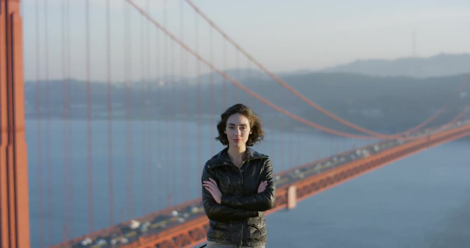 A woman stands in front of the golden gate bridge with her arms crossed