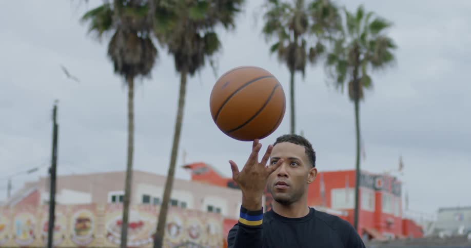 A black man spins a basketball on this finger