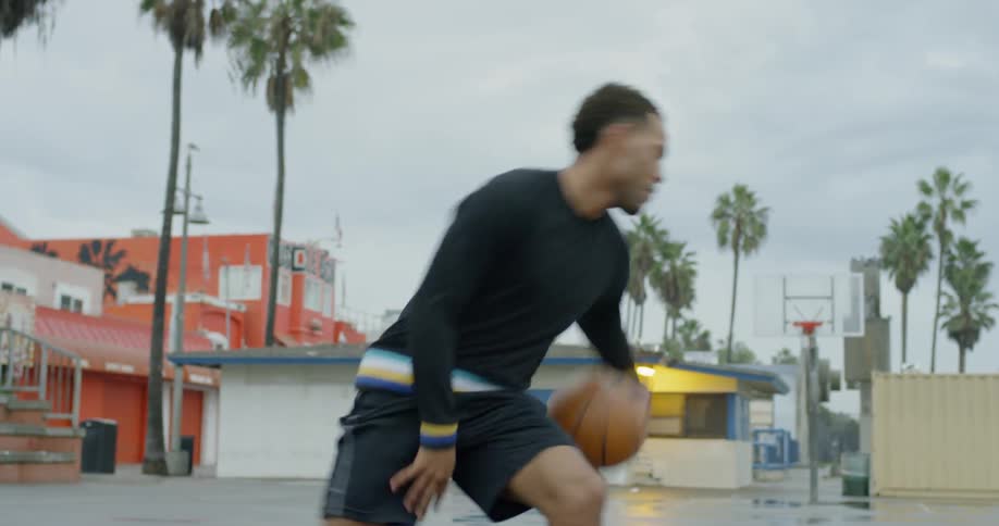 A black male dribbles a basketball between his legs on an outdoor court and then take a shot with the ball
