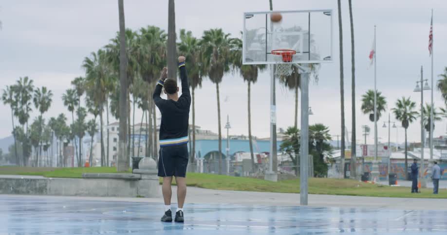 A man dribbles the ball briefly before throwing a basketball at the hoop and making the shot on an outdoor basketball court