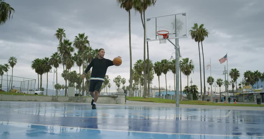 A black male dribbles a basketball on a court before going in for a layup and shooting the ball in the hoop