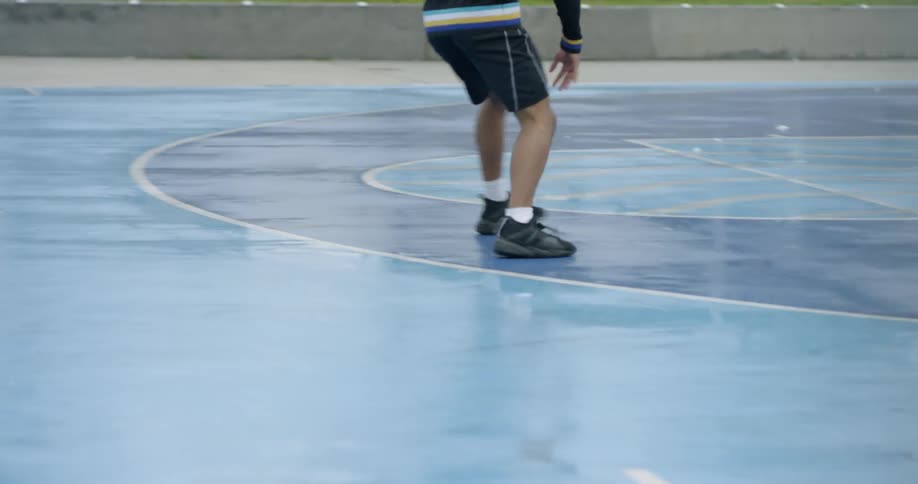 A black man dribbles and moves quickly on a wet basketball court