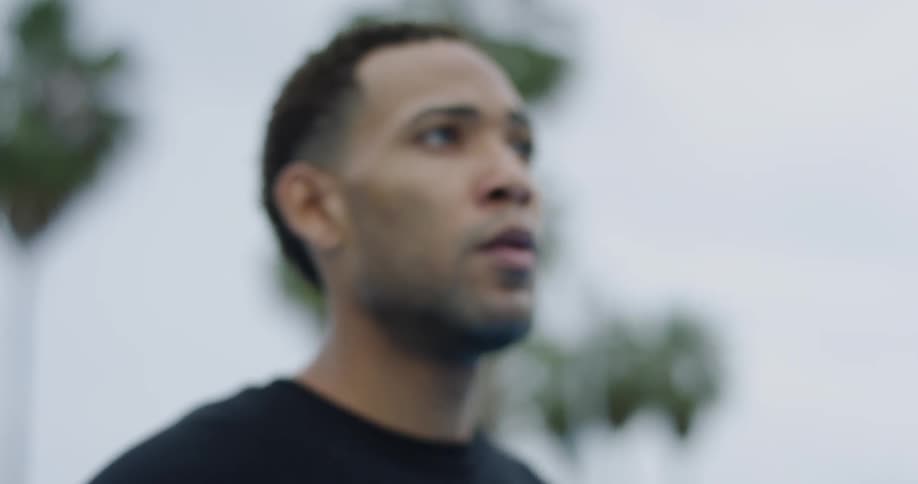 A black man stands outdoors and looks off into the distance