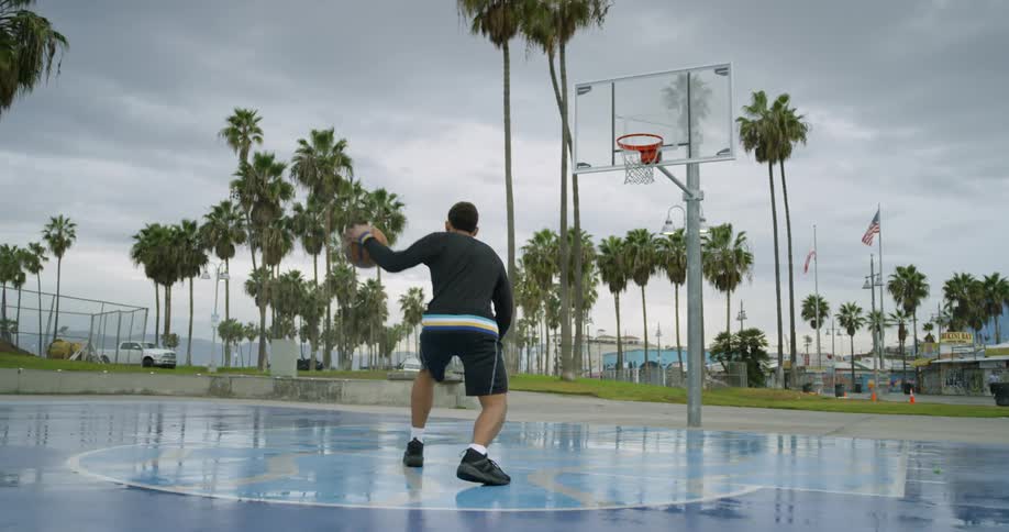Man dribbling basketball on court in park