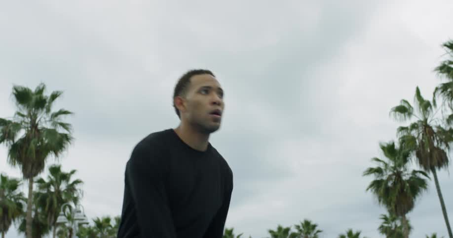 Man bouncing a basketball outside under palm trees