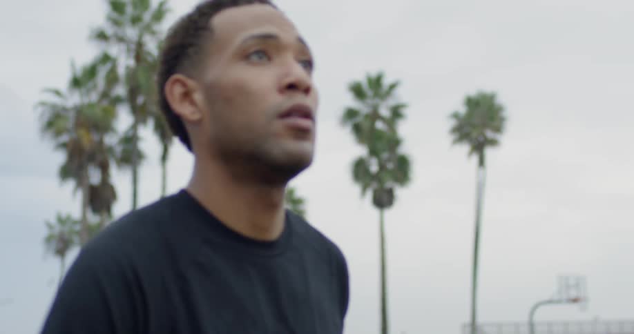 A black male looks ahead intensely on a basketball court and then shoots the ball with his right hand