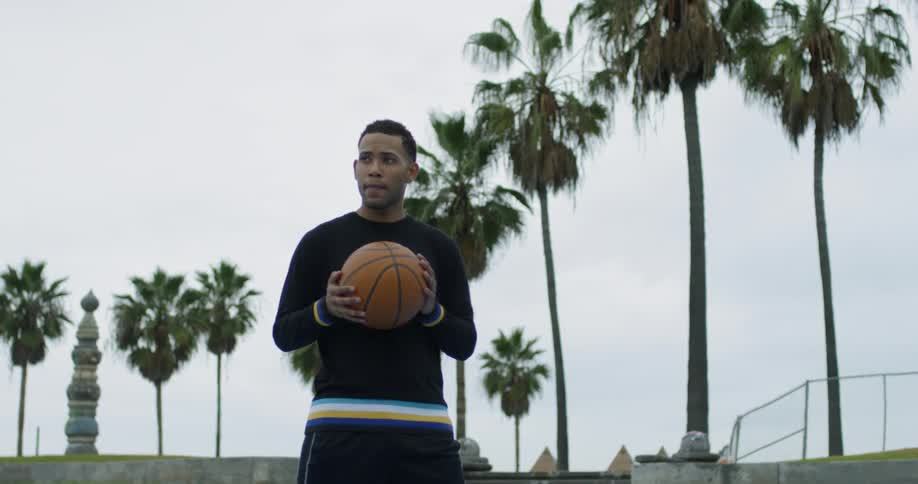 A black man holds a basketball while looking off into the distance
