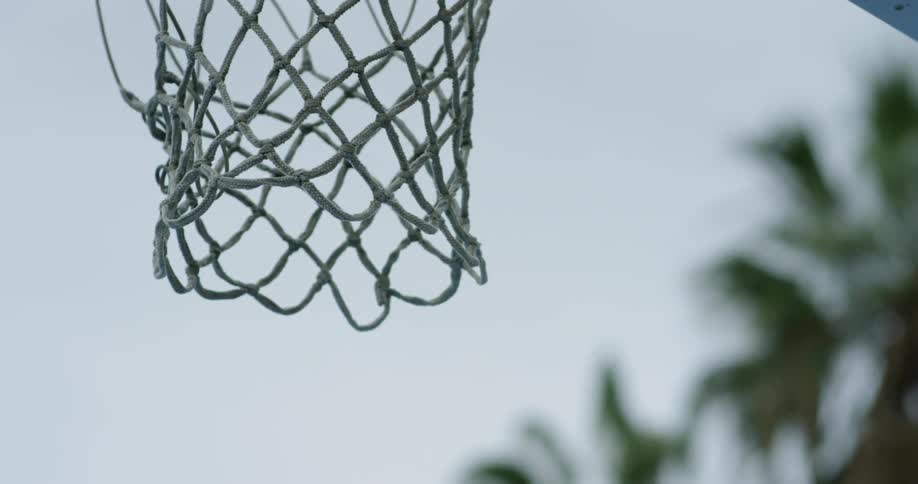 A basketball falls through the net of a basketball hoop on an outdoor court